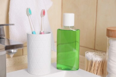 Photo of Fresh mouthwash in bottle and holder with toothbrushes on sink in bathroom, closeup