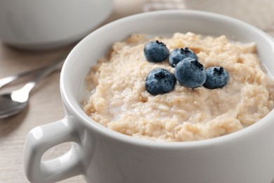 Tasty oatmeal porridge with blueberries in bowl on table, closeup