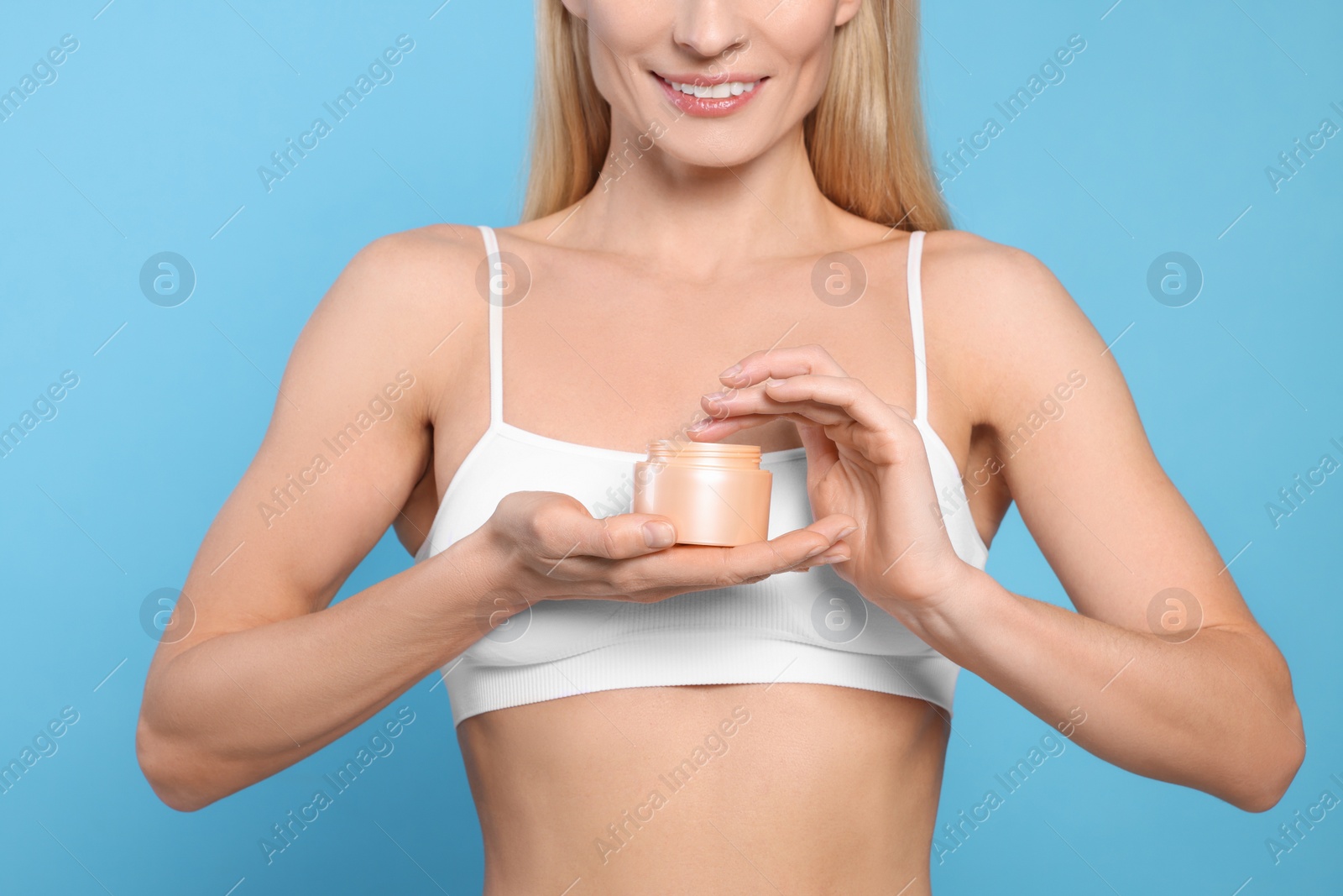 Photo of Woman with jar of body cream on light blue background, closeup