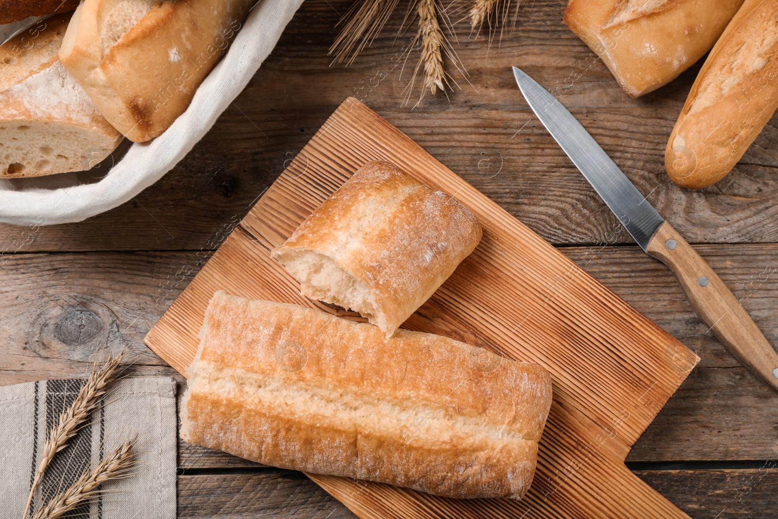 Photo of Fresh tasty baguettes, knife and spikelets on wooden table, flat lay