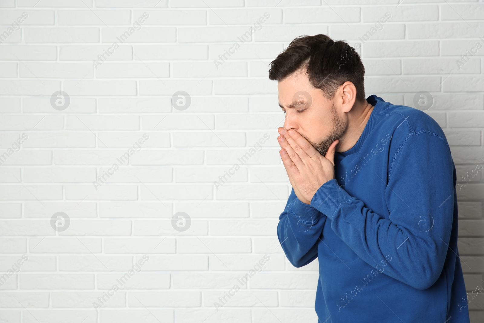 Photo of Man suffering from cough near brick wall. Space for text