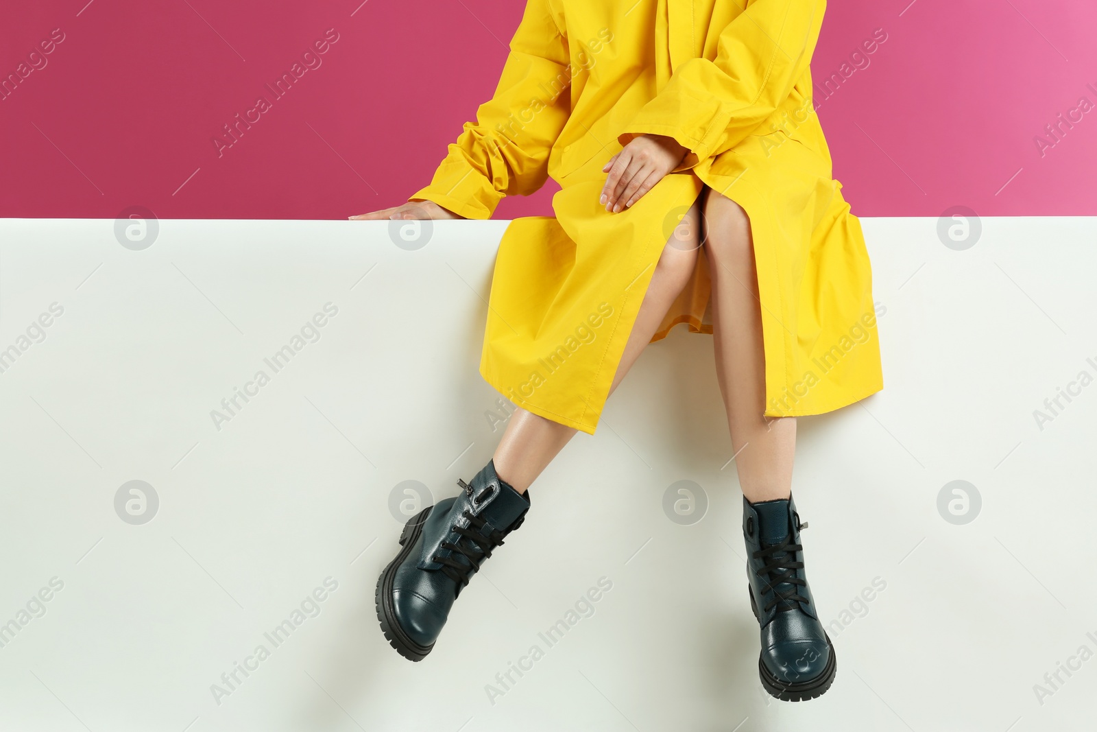 Photo of Woman in stylish boots sitting on color background, closeup