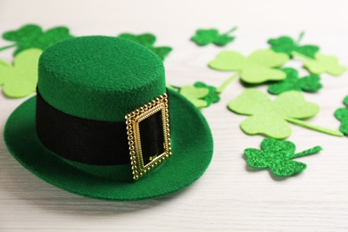 Leprechaun hat and decorative clover leaves on white wooden table, space for text. St Patrick's Day celebration