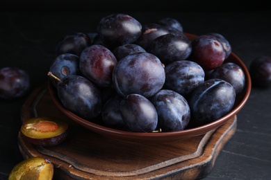 Delicious ripe plums in bowl on black table