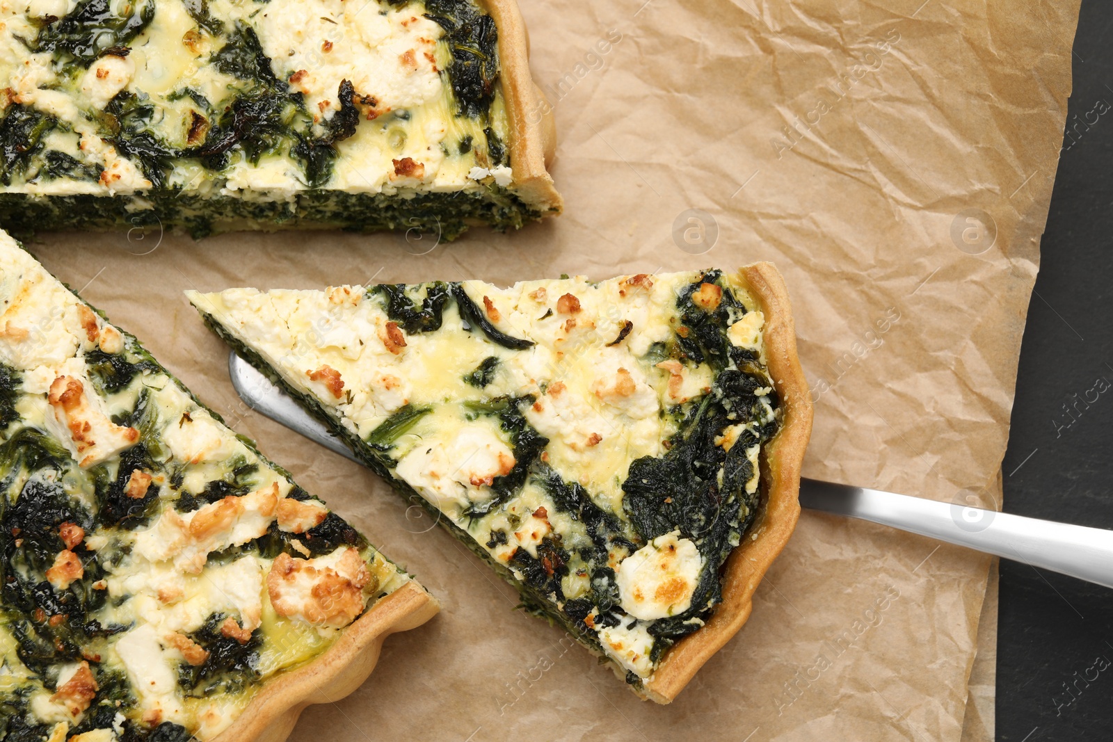 Photo of Taking piece of delicious homemade spinach quiche on parchment paper, flat lay