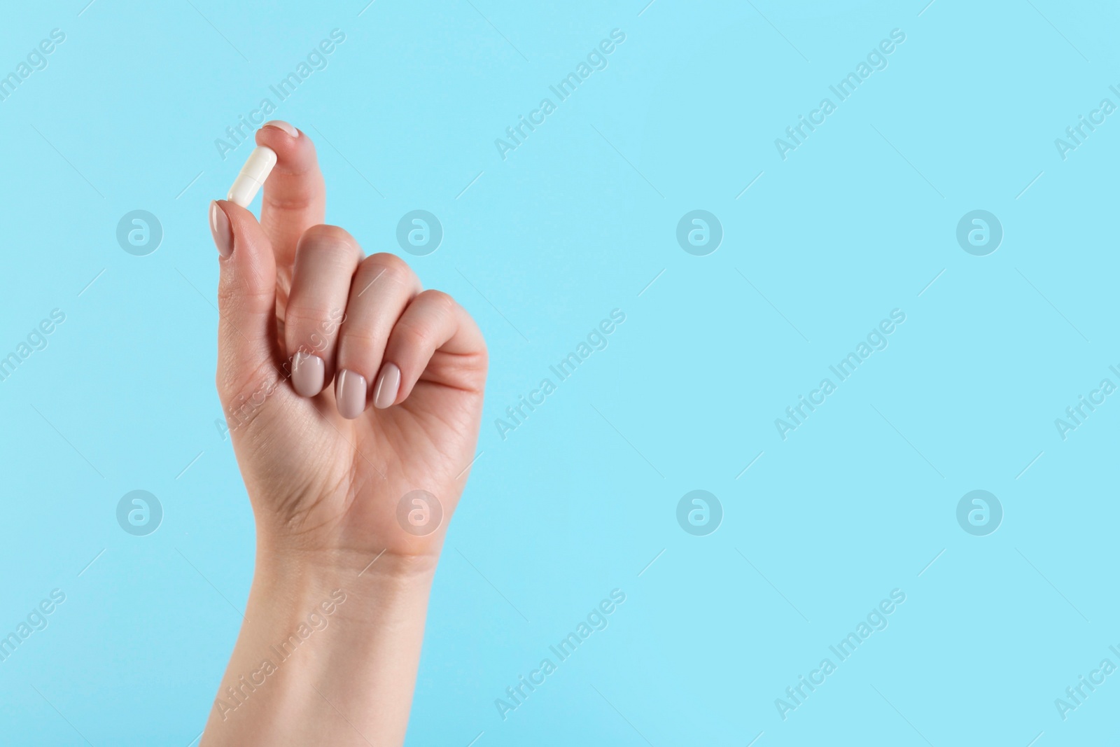 Photo of Woman holding vitamin capsule on light blue background, closeup with space for text. Health supplement