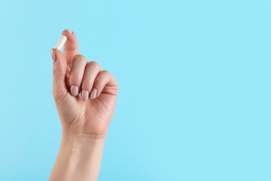 Photo of Woman holding vitamin capsule on light blue background, closeup with space for text. Health supplement