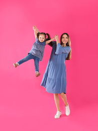 Photo of Young mother and little daughter having fun on pink background