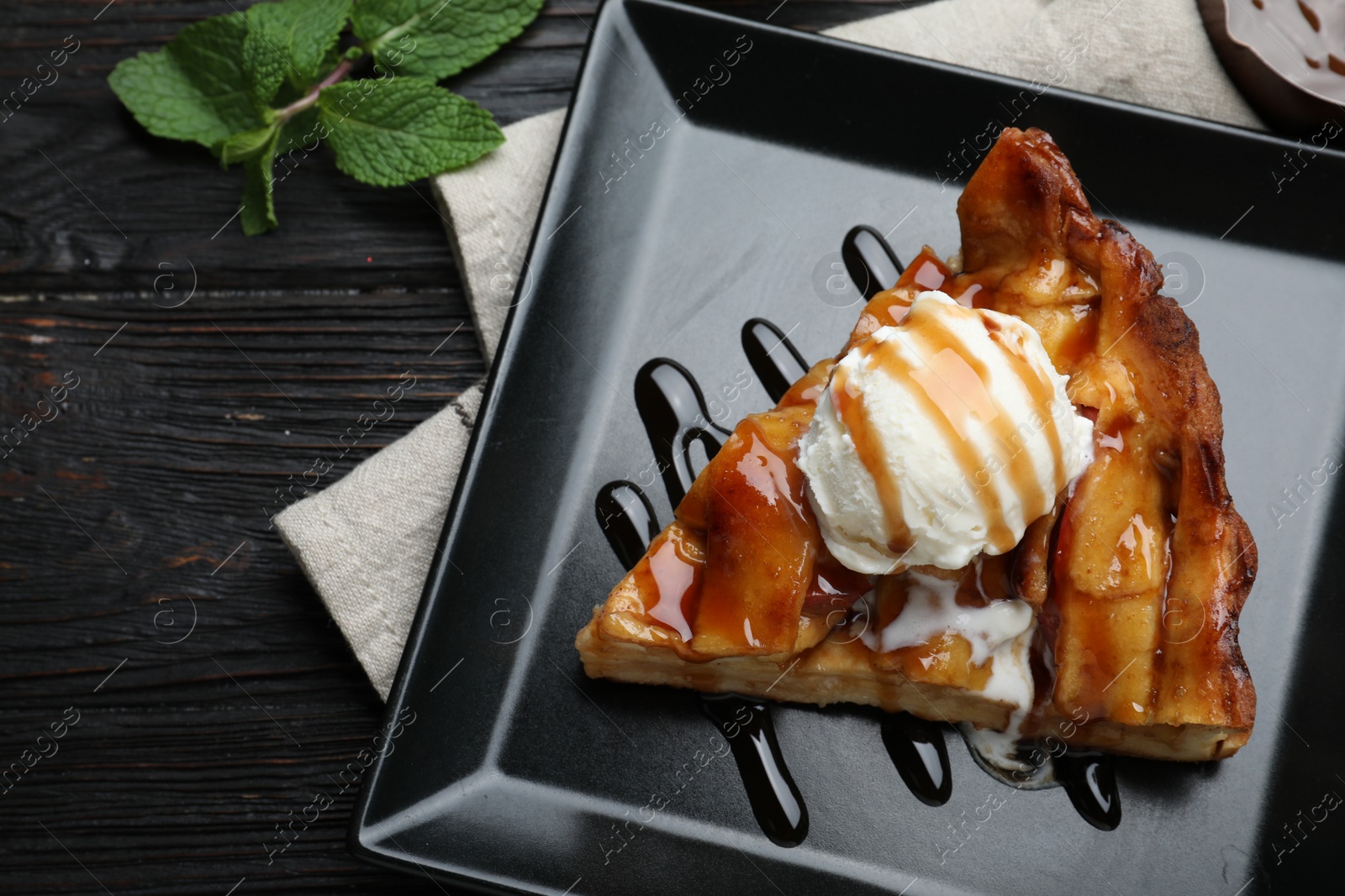 Photo of Slice of traditional apple pie with ice cream on black wooden table, flat lay