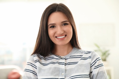 Photo of Young woman looking at camera and using video chat in home office