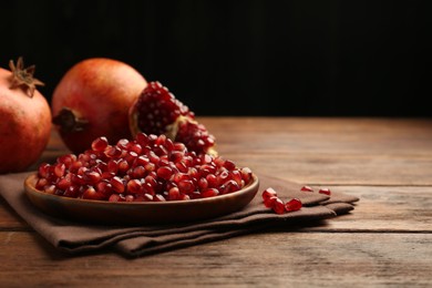 Photo of Ripe juicy pomegranates and grains on wooden table. Space for text