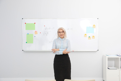 Mature teacher near whiteboard in modern classroom