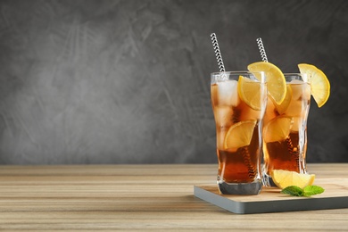 Photo of Glasses of tasty ice tea with lemon on wooden table against grey background, space for text