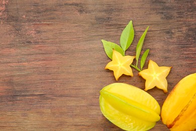 Photo of Cut and whole delicious ripe carambolas with leaves on wooden table, flat lay. Space for text