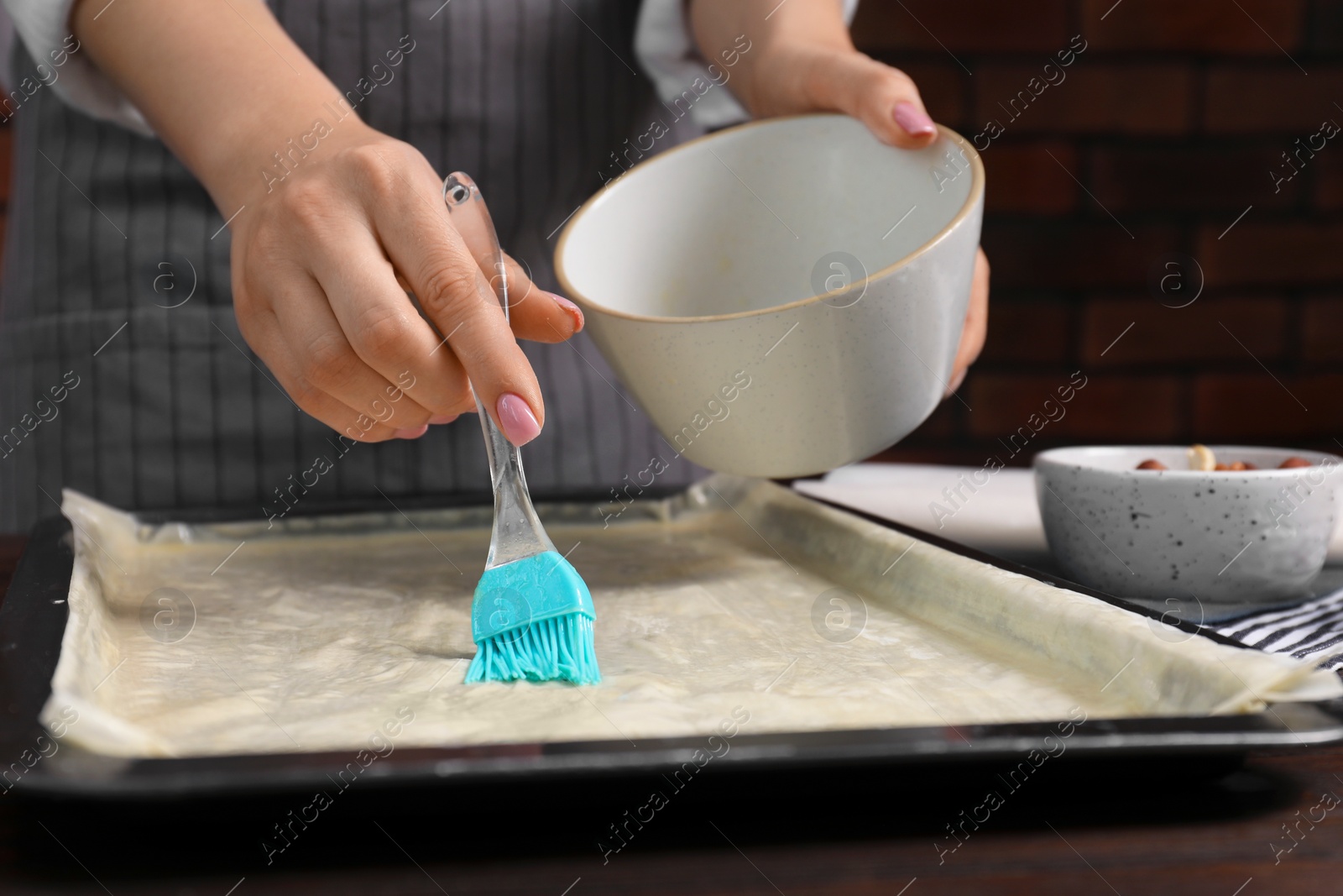 Photo of Making delicious baklava. Woman buttering dough at table, closeup