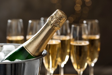 Bottle of champagne in bucket with ice and glasses on blurred background, closeup. Space for text