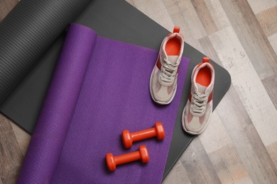 Photo of Dumbbells, sneakers and mats on wooden floor, above view