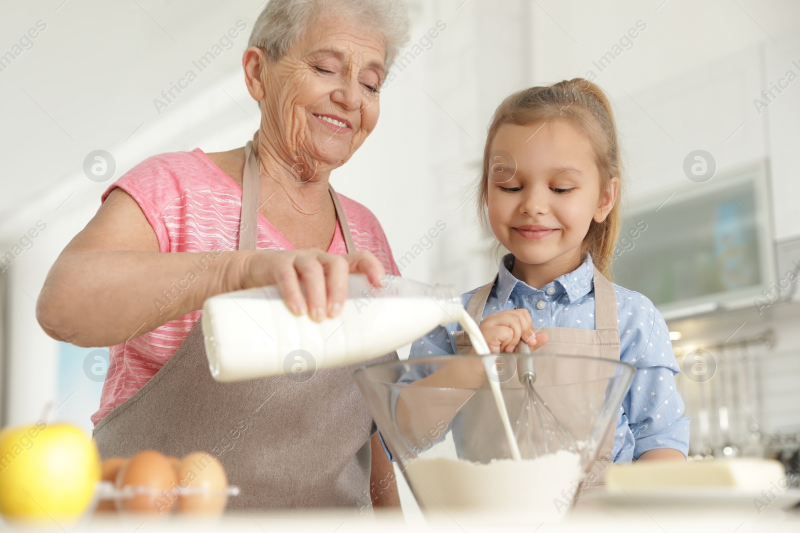 Photo of Cute girl and her grandmother cooking in kitchen