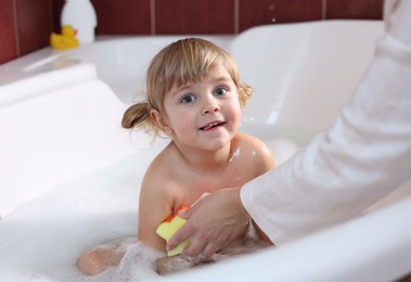 Photo of Mother washing her smiling daughter with sponge in bathtub, closeup