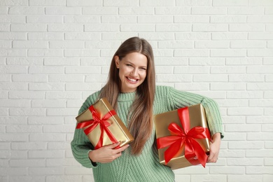 Photo of Happy young woman with Christmas gifts near white brick wall