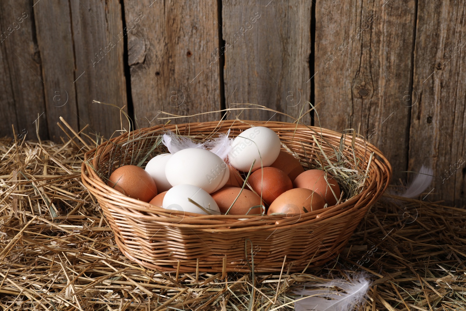 Photo of Fresh chicken eggs in wicker basket on dried straw near wooden wall