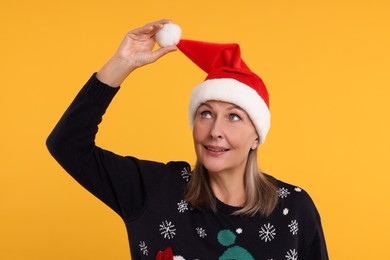Happy senior woman in Christmas sweater and Santa hat on orange background