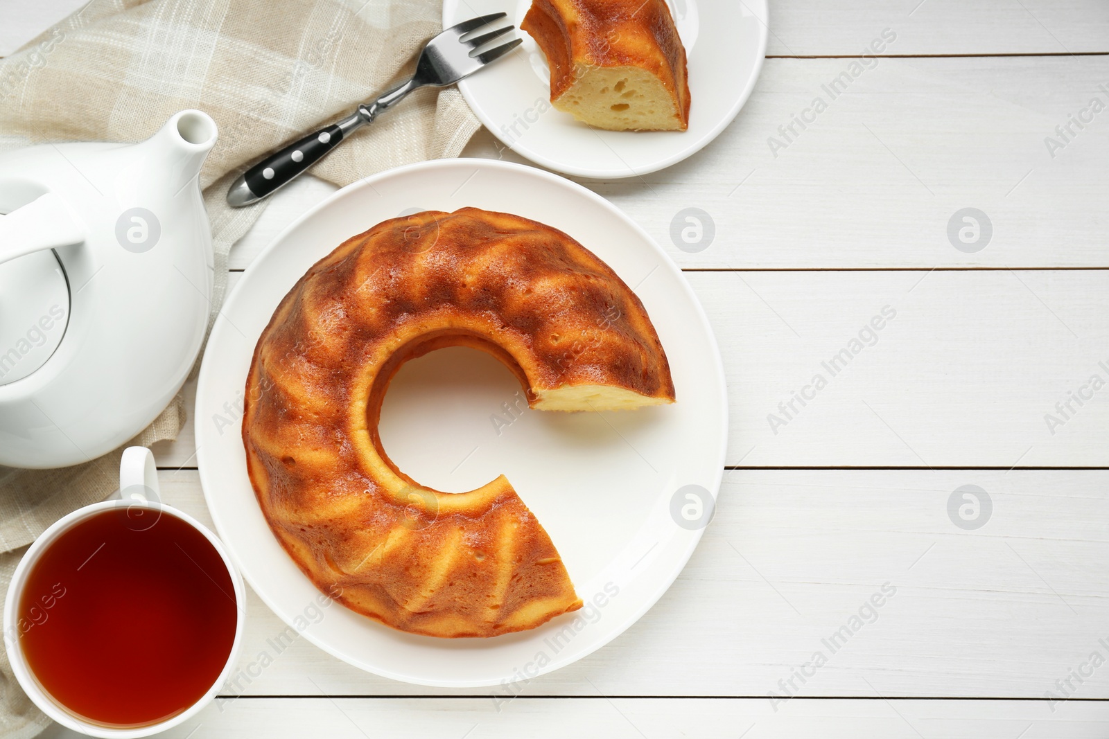 Photo of Delicious homemade yogurt cake and cup tea on white wooden table, flat lay. Space for text