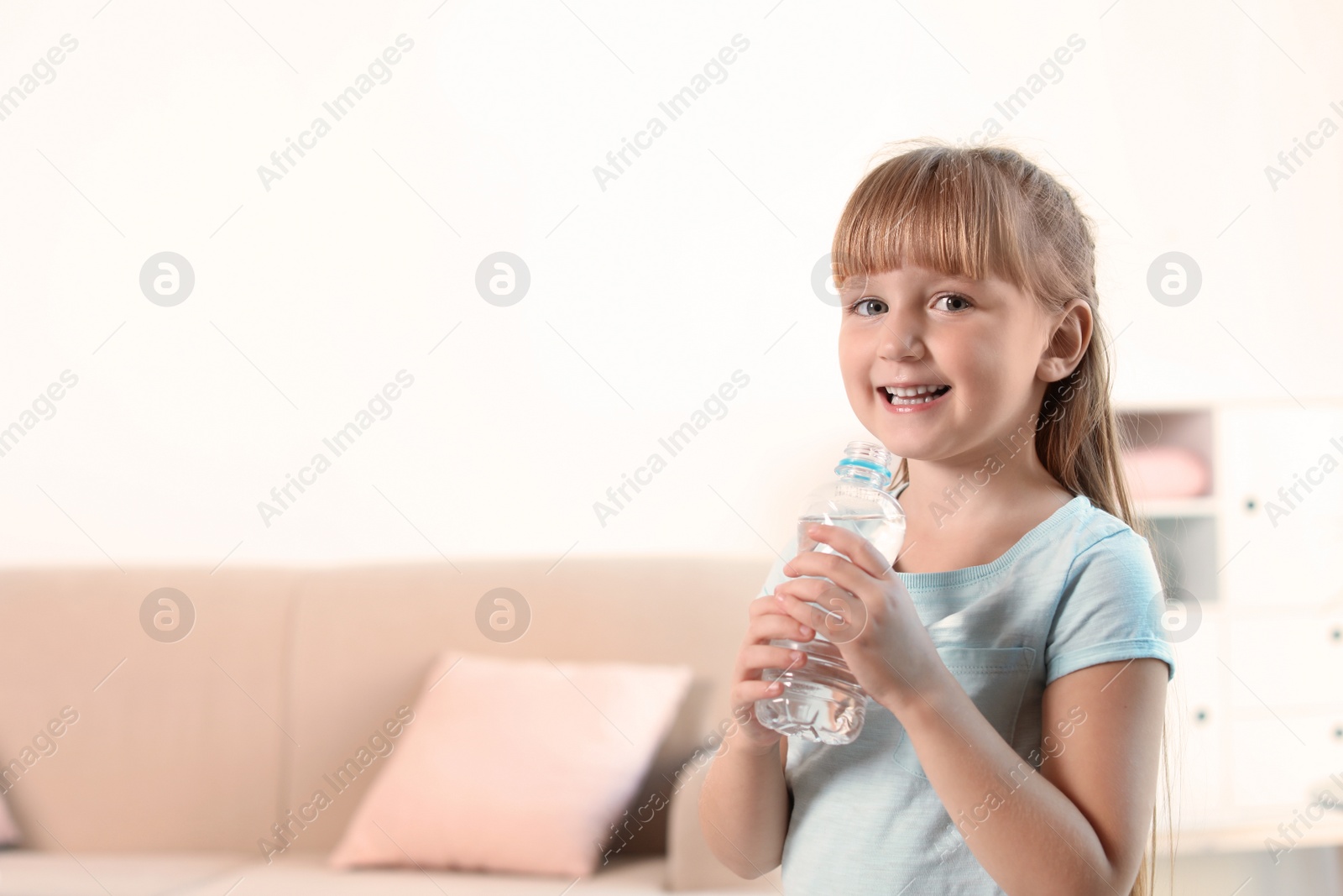 Photo of Cute little girl holding bottle with water at home. Space for text