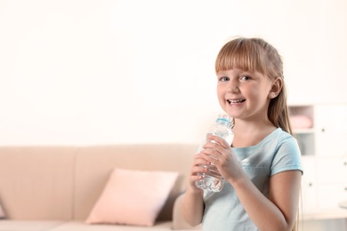 Photo of Cute little girl holding bottle with water at home. Space for text