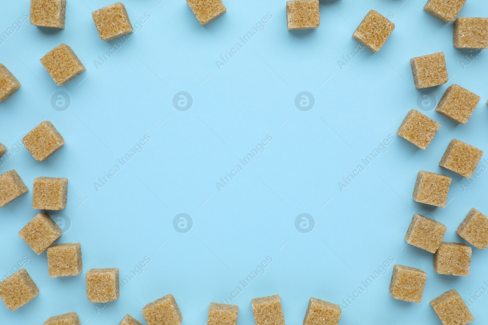 Photo of Frame of brown sugar cubes on light blue background, flat lay. Space for text