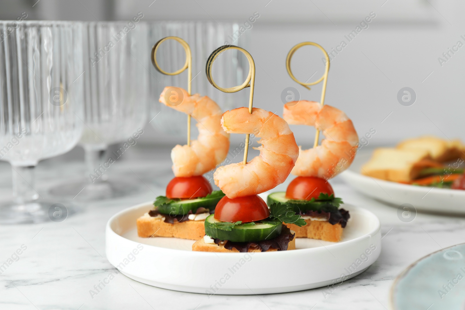 Photo of Tasty canapes with shrimps, cucumber, greens and tomatoes on white marble table, closeup