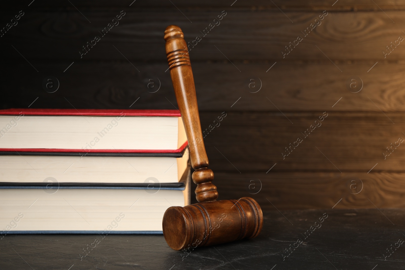 Photo of Wooden gavel and stack of books on dark textured table. Space for text