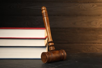 Photo of Wooden gavel and stack of books on dark textured table. Space for text