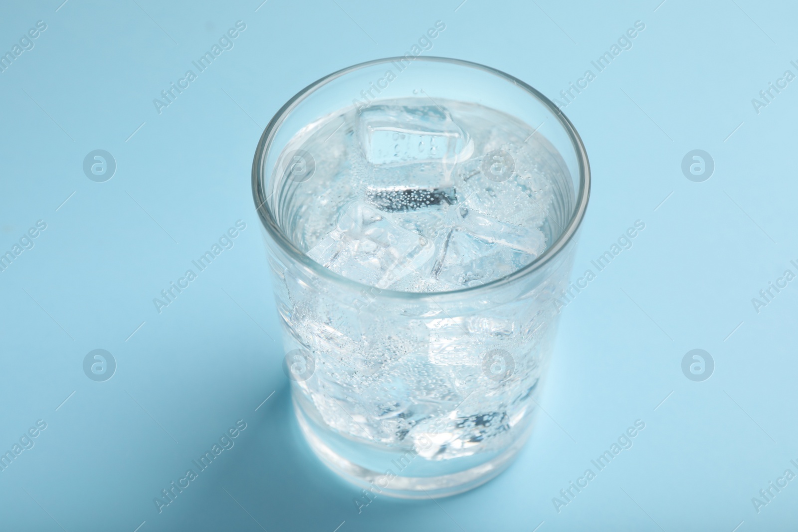 Photo of Glass of soda water with ice on light blue background, closeup