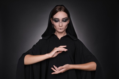 Photo of Mysterious witch in mantle with hood on dark background