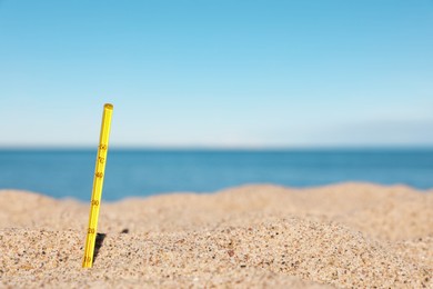 Photo of Yellow weather thermometer in sand near sea, space for text