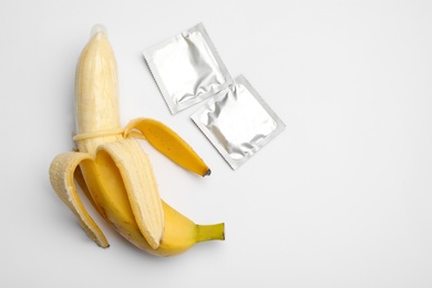 Photo of Banana with condoms on white background, top view. Safe sex