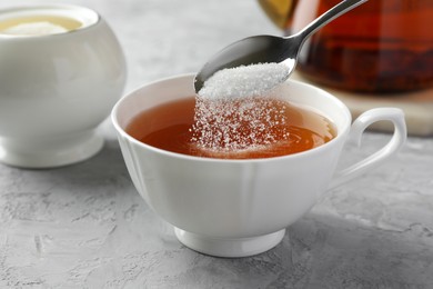 Adding sugar into cup of tea at grey textured table, closeup