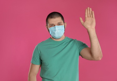 Photo of Man in protective mask showing hello gesture on pink background. Keeping social distance during coronavirus pandemic
