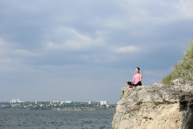 Photo of Young woman meditating on cliff near river. Space for text
