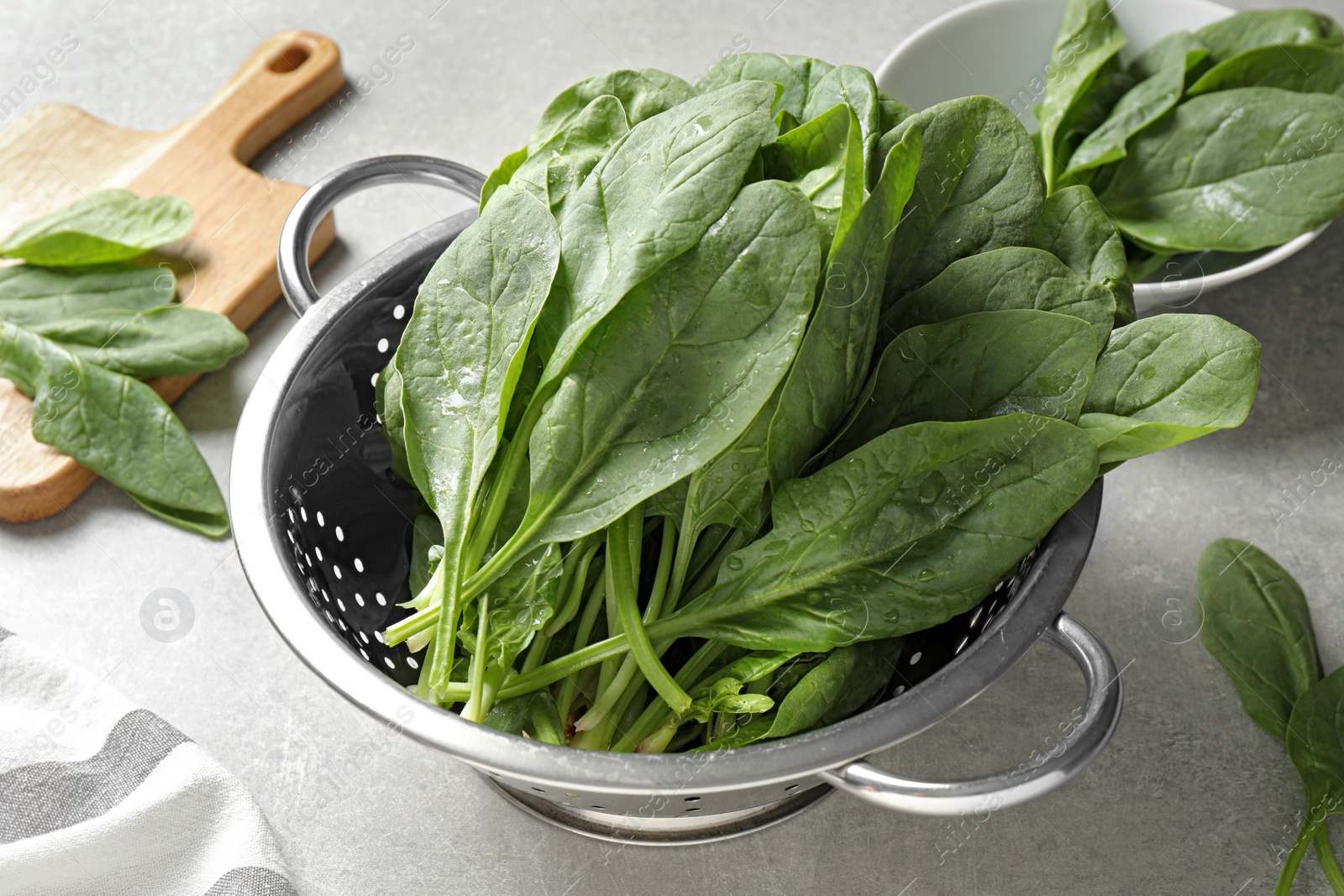 Photo of Colander with fresh green healthy spinach on grey table