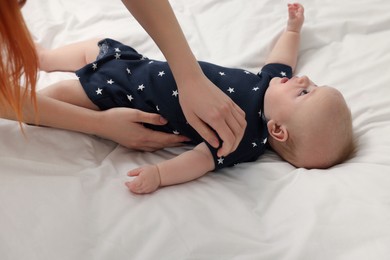 Mother putting clothes on her baby at bed, closeup