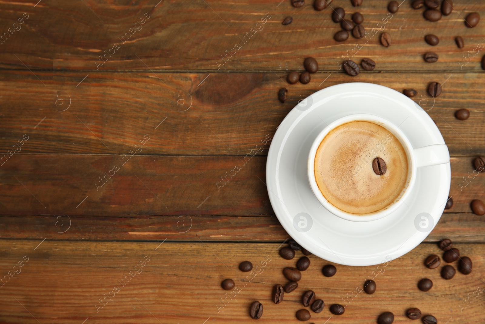 Photo of Cup of tasty coffee and beans on wooden table, flat lay. Space for text