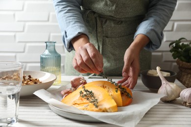 Photo of Woman putting aromatic thyme branches onto fresh ripe pumpkin slices at table, closeup