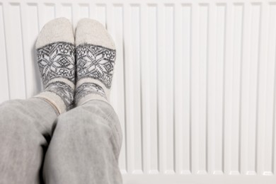 Photo of Woman warming feet near heating radiator, closeup