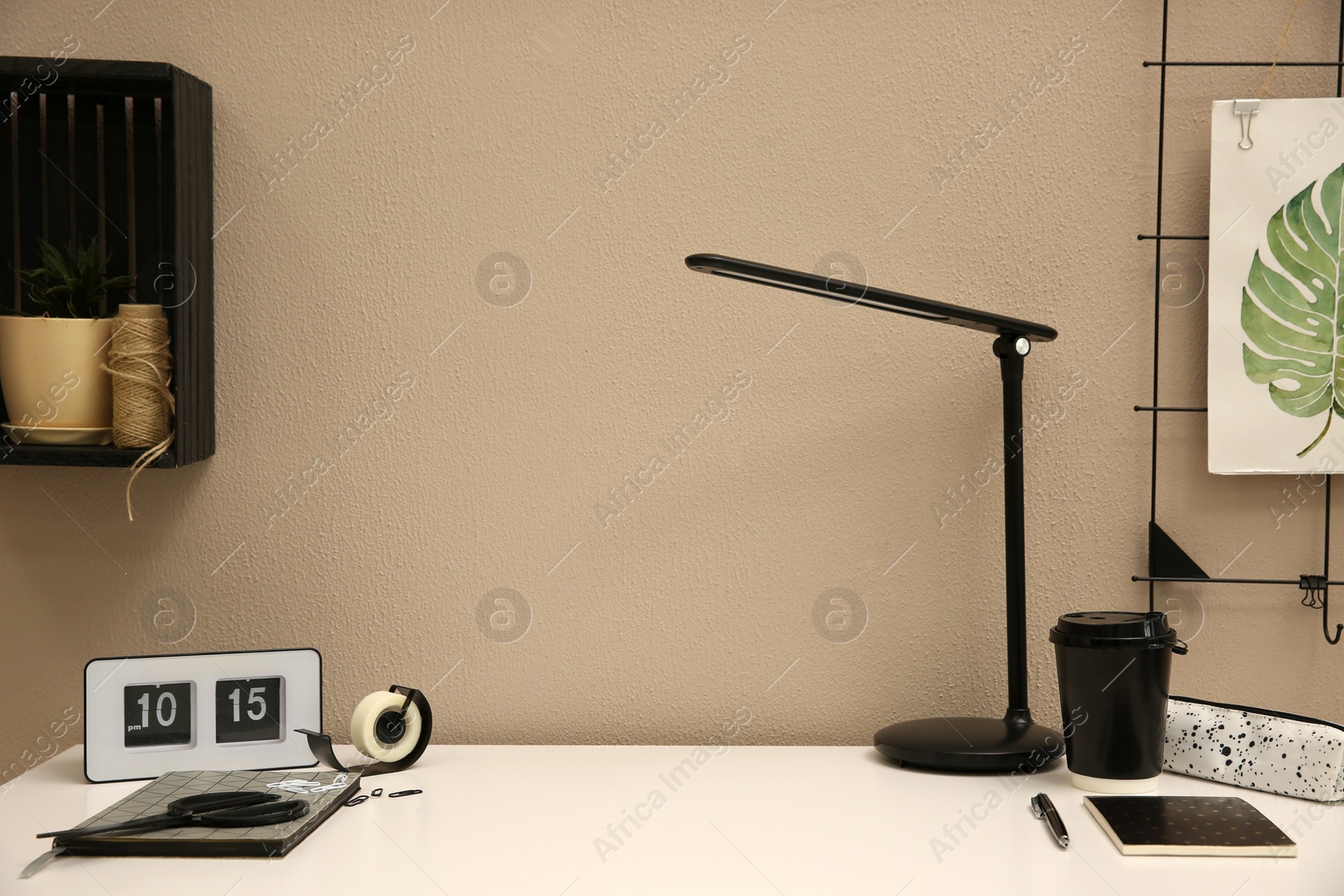 Photo of Stylish workplace with stationery on white desk near beige wall. Interior design