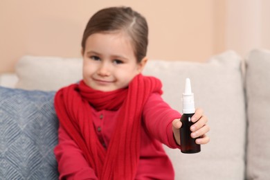 Photo of Cute little girl showing nasal spray indoors, focus on hand