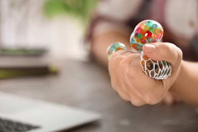 Photo of Woman squeezing colorful slime in office, closeup. Antistress toy