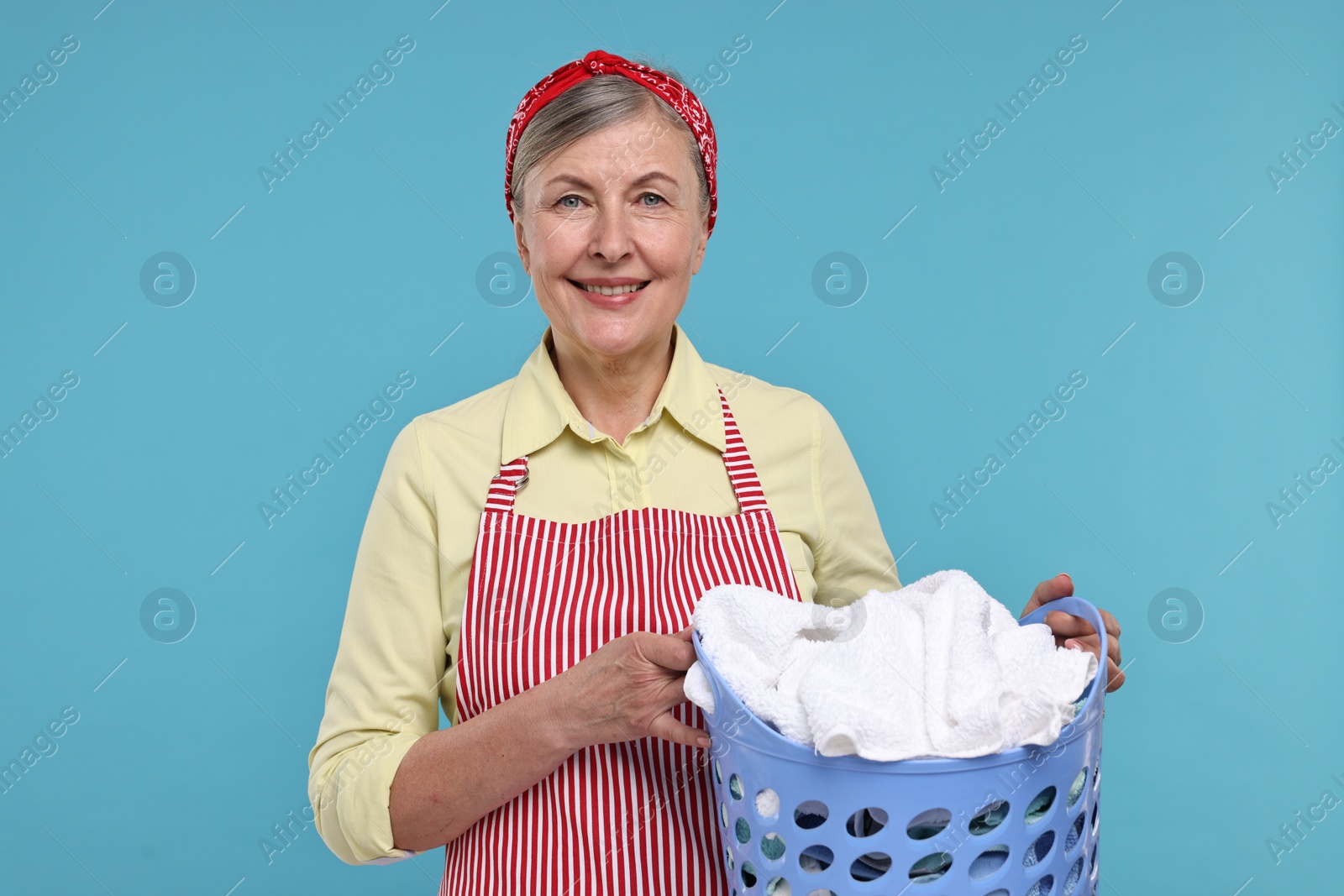 Photo of Happy housewife with basket full of laundry on light blue background