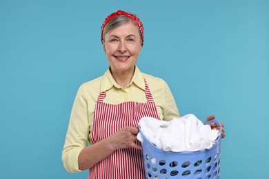 Photo of Happy housewife with basket full of laundry on light blue background